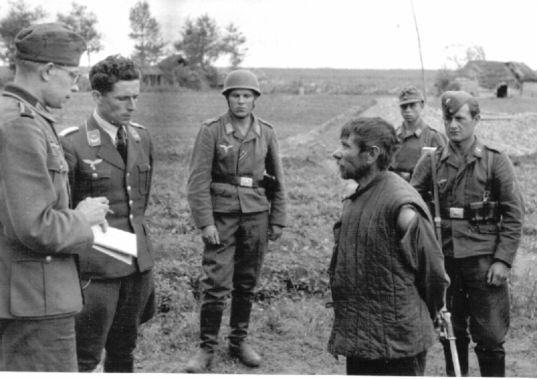 Немецкие военные допрашивают местного жителя, подозреваемого в участии в партизанском отряде.​ Новгородская область, лето 1942 года