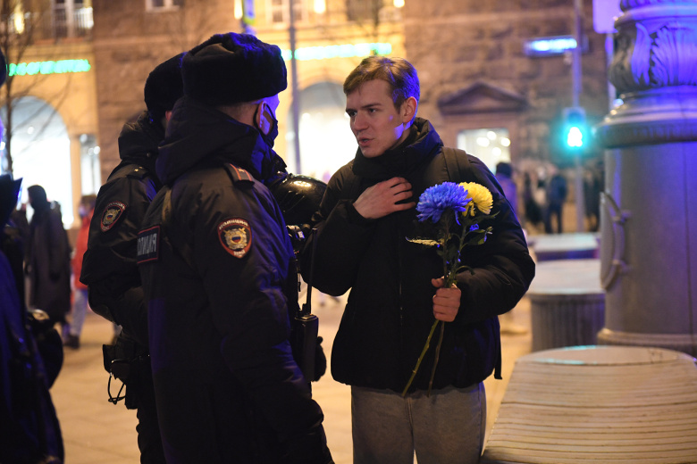 Участник антивоенной акции объясняется с росгвардейцами, у него в руке хризантемы, окрашенные в цвета украинского флага. Пушкинская площадь, 25 февраля 2022 года. Фото: Komsomolskaya Pravda / Global Look Press