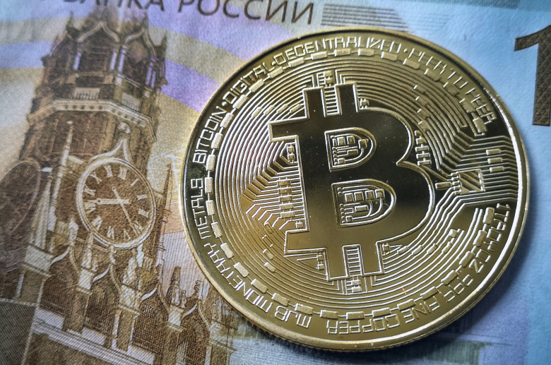 Биткоин-токен рядом со сторублевой купюрой.