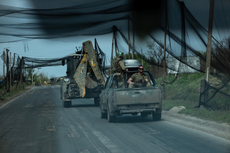 Украинские военнослужащие батальона «Черный ворон» едут в транспортных средствах по дороге, покрытой сеткой для защиты техники от атак беспилотников.