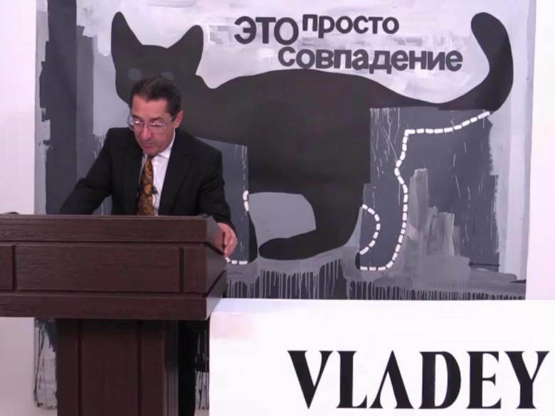 Владимир Овчаренко проводит торги «Сливки» аукциона Vladey из серии «Все по 100» на фоне одного из лотов – котика Валерия Чтака